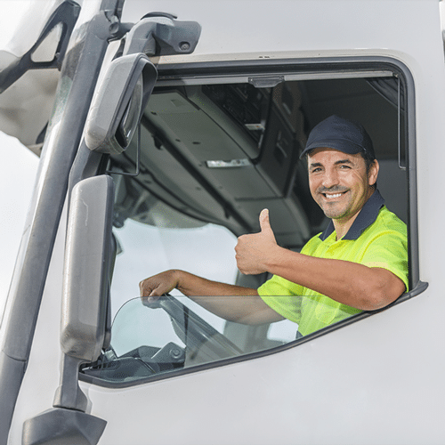 A man in a high-visibility shirt and cap gives a thumbs-up while sitting in the driver's seat of a truck, proudly representing carrier solutions.