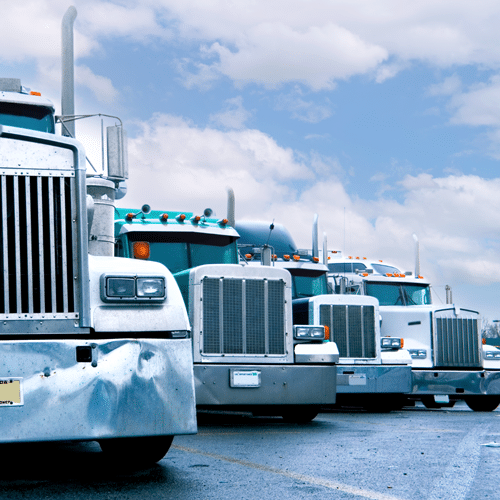 A row of parked semi-trucks under a cloudy sky, viewed from the front, represents the strength of carrier solutions in action.