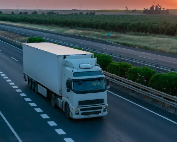 LTL vs. FTL Freight Shipping: What's the Difference? - Freight Brokerage, Freight Agents & LTL Freight Shipping A white semi-truck, part of an efficient freight shipping operation, cruises down the highway, silhouetted against a vibrant sunset with green fields and trees in the background.