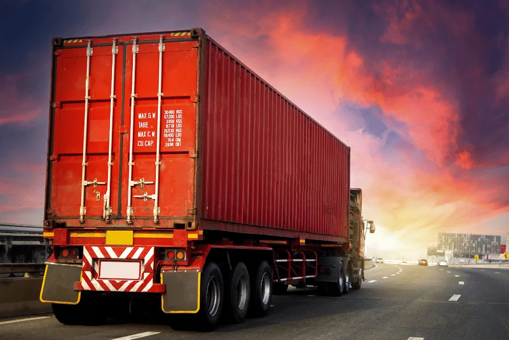 A red cargo truck with a shipping container drives on a highway under a dramatic, colorful sunset sky, symbolizing the journey of logistics process automation in modern supply chains.